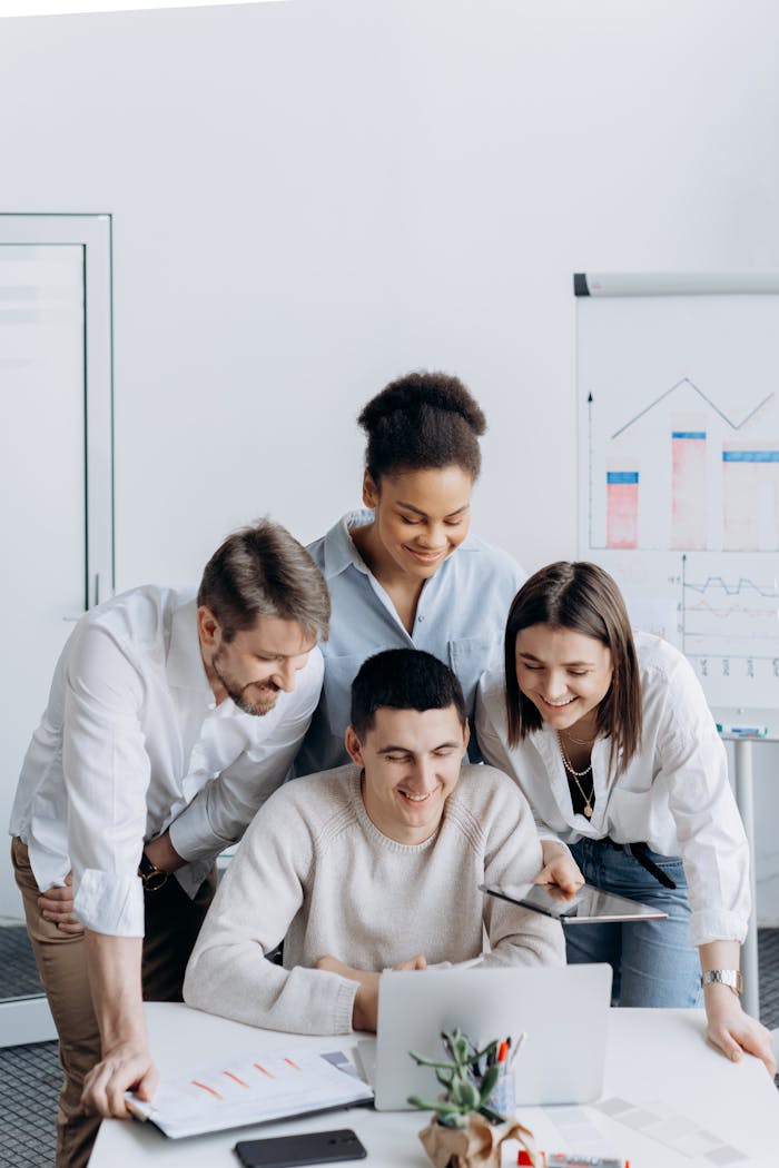 Diverse team of adults collaborating around a laptop in a modern office setting.